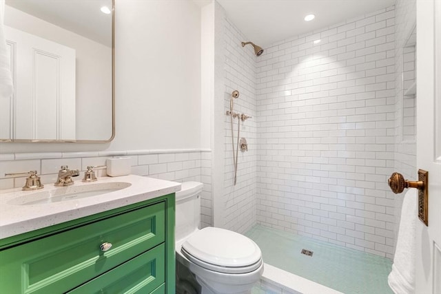 bathroom with vanity, a tile shower, wainscoting, tile walls, and toilet