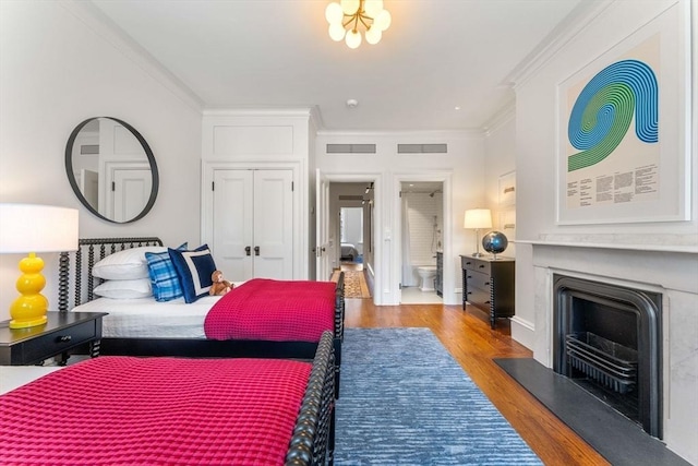 bedroom with wood finished floors, visible vents, a fireplace, ornamental molding, and a closet