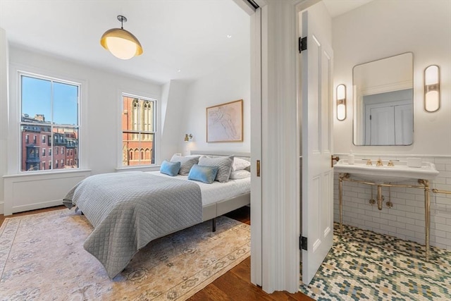 bedroom featuring a sink, wood finished floors, connected bathroom, tile walls, and wainscoting