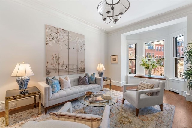 living area with a notable chandelier, wood finished floors, baseboards, and ornamental molding