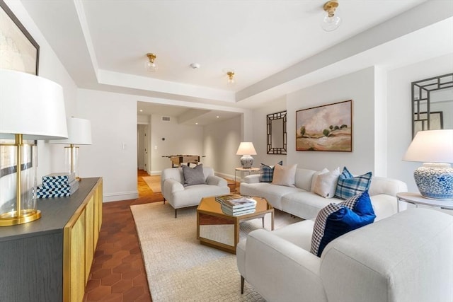 living room featuring a tray ceiling, baseboards, and dark tile patterned flooring