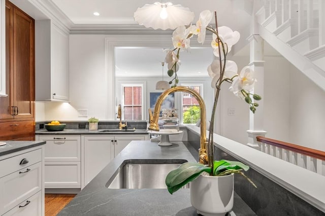 kitchen featuring a sink, dark countertops, ornamental molding, and white cabinets