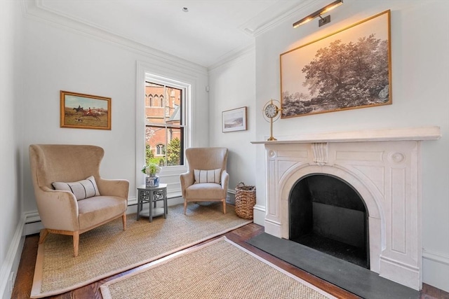 sitting room with a baseboard heating unit, wood finished floors, a fireplace, crown molding, and baseboards