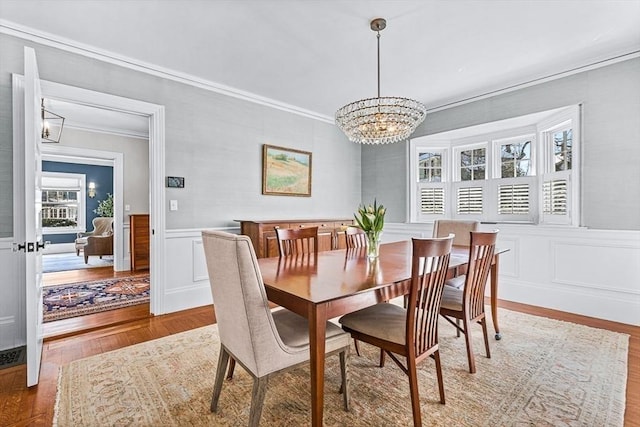 dining space with wainscoting, ornamental molding, wood finished floors, a chandelier, and a decorative wall