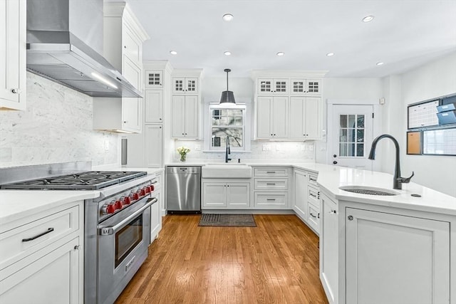 kitchen featuring appliances with stainless steel finishes, decorative light fixtures, light countertops, wall chimney range hood, and a sink