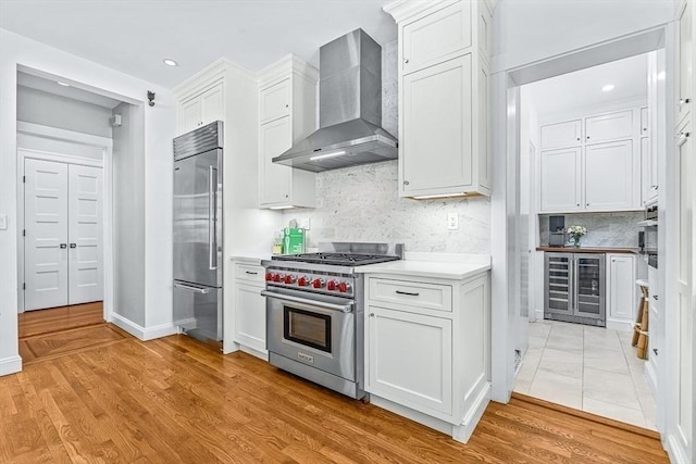 kitchen featuring high end appliances, wine cooler, white cabinets, and wall chimney range hood