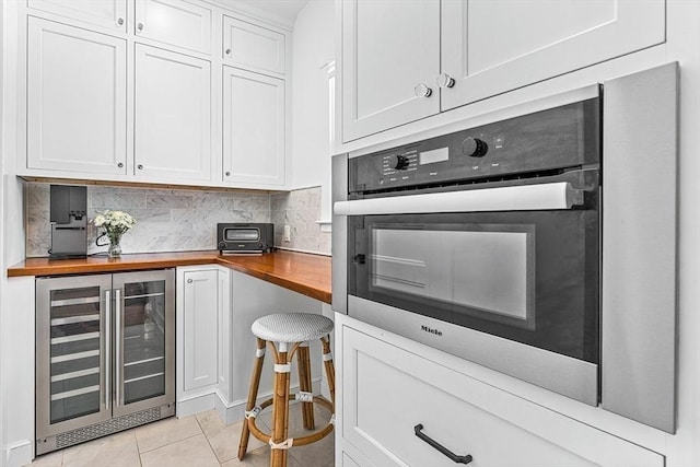 kitchen featuring wine cooler, oven, butcher block counters, white cabinets, and decorative backsplash