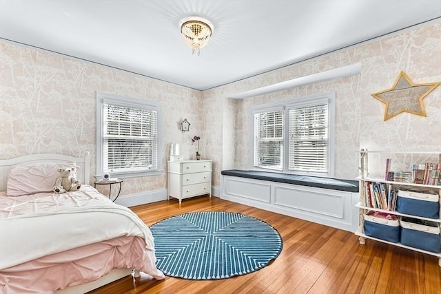 bedroom featuring baseboards, wood finished floors, and wallpapered walls