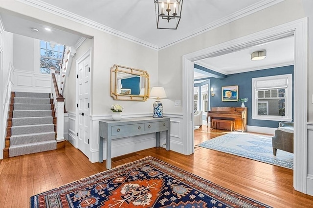 foyer featuring a notable chandelier, crown molding, a decorative wall, stairway, and wood finished floors