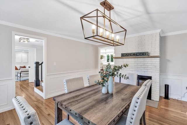 dining space with a chandelier, ornamental molding, light hardwood / wood-style floors, and a brick fireplace