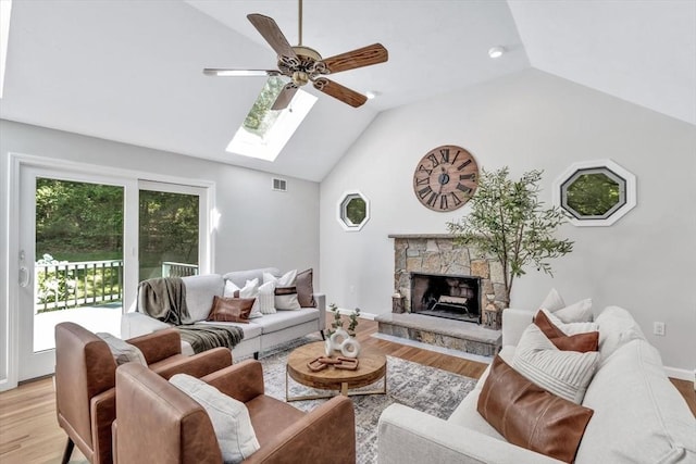 living room with a stone fireplace, ceiling fan, light hardwood / wood-style floors, and lofted ceiling with skylight