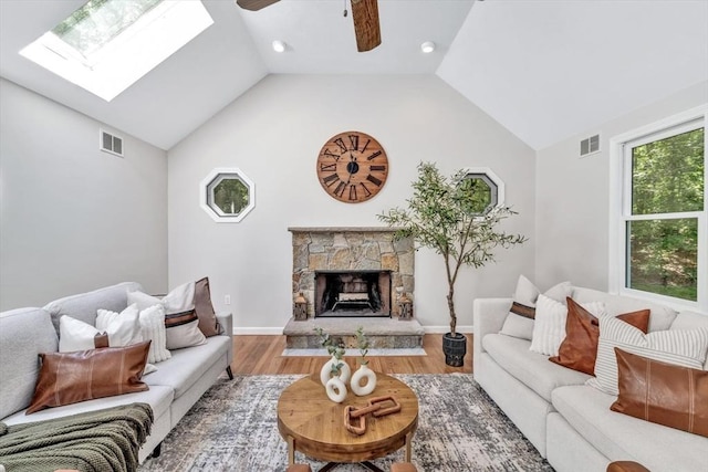 living room featuring hardwood / wood-style flooring, ceiling fan, vaulted ceiling with skylight, and a fireplace