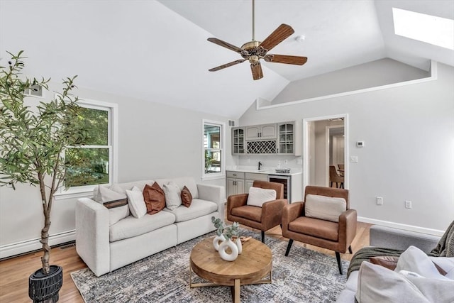 living room with ceiling fan, beverage cooler, baseboard heating, lofted ceiling with skylight, and light wood-type flooring