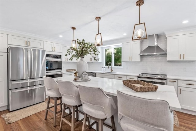 kitchen with pendant lighting, wall chimney exhaust hood, decorative backsplash, white cabinetry, and stainless steel appliances