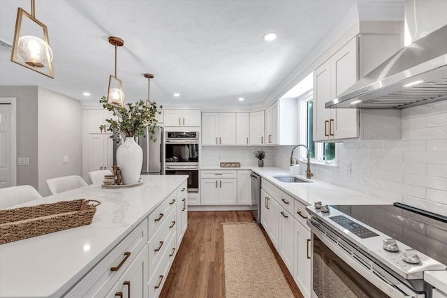 kitchen with white cabinetry, sink, wall chimney range hood, decorative light fixtures, and appliances with stainless steel finishes