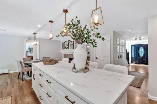 kitchen with a kitchen island, decorative light fixtures, light hardwood / wood-style floors, light stone counters, and white cabinetry