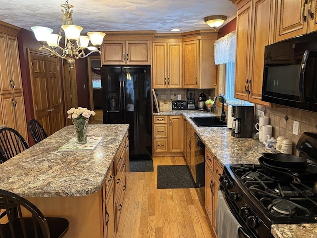 kitchen featuring light stone countertops, a chandelier, a sink, light wood-style flooring, and black appliances