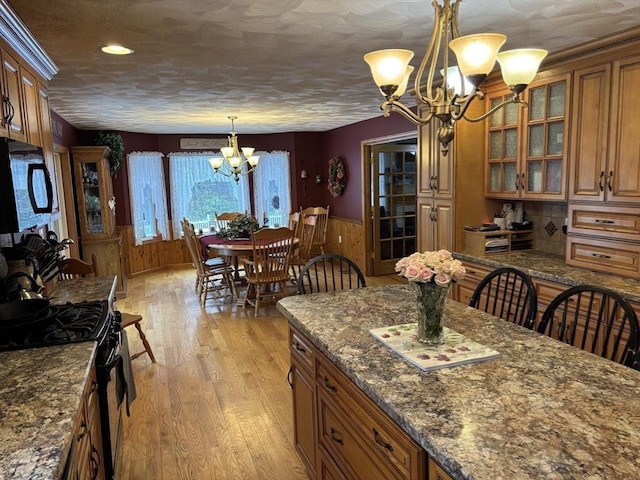 kitchen with a notable chandelier, black microwave, brown cabinetry, light wood-style flooring, and gas range