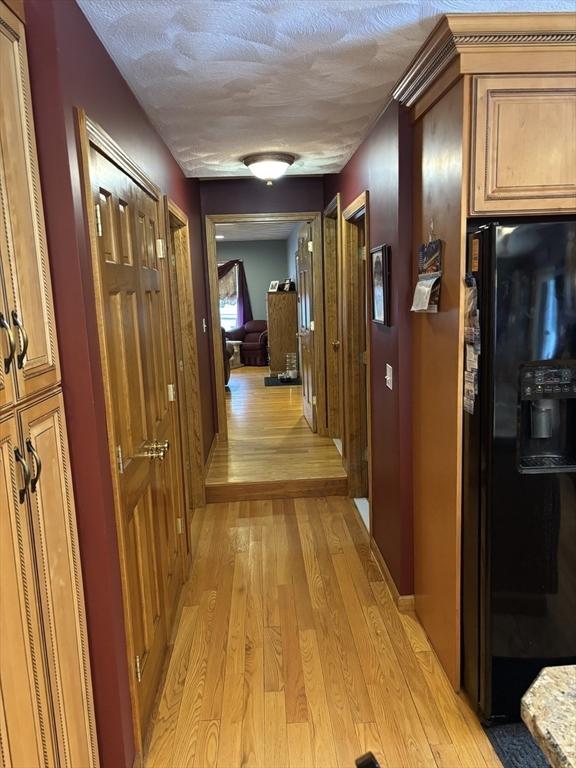 hallway featuring baseboards, light wood finished floors, and a textured ceiling