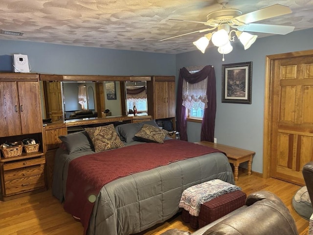 bedroom featuring ceiling fan, a textured ceiling, visible vents, and light wood-style flooring