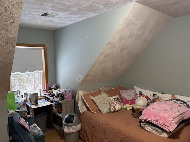 bedroom featuring a textured ceiling, visible vents, wood finished floors, and vaulted ceiling