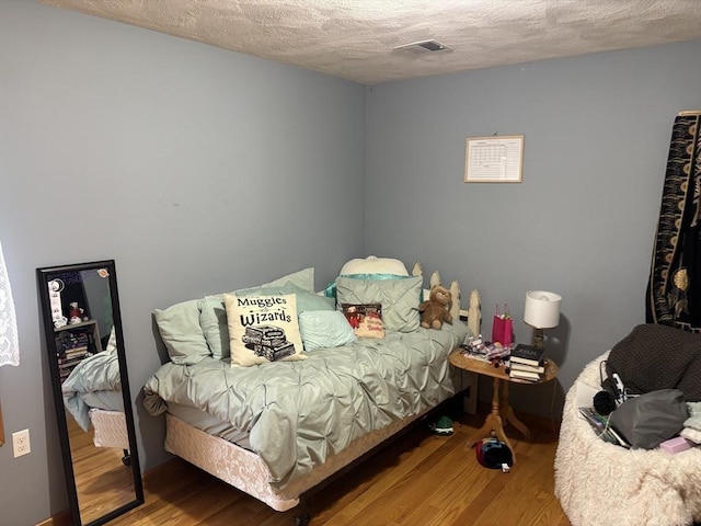 bedroom with a textured ceiling, visible vents, and wood finished floors