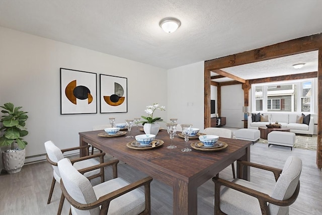 dining room featuring hardwood / wood-style flooring, a baseboard heating unit, a textured ceiling, and beam ceiling