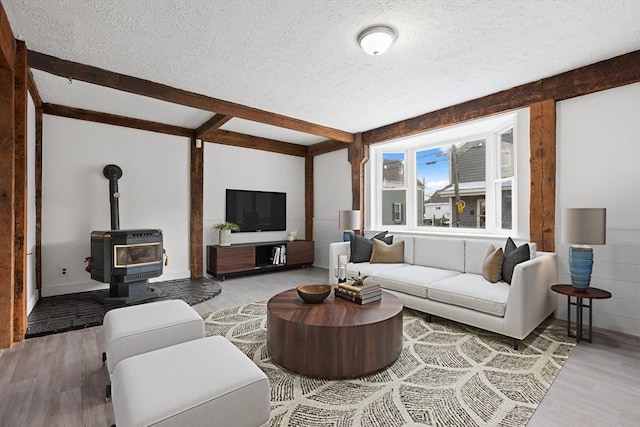 living room featuring beam ceiling, light hardwood / wood-style floors, a textured ceiling, and a wood stove