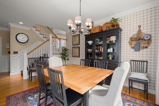 dining room with stairway, wood finished floors, ornamental molding, and wallpapered walls