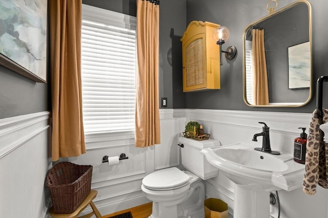 bathroom with a wealth of natural light, a decorative wall, wainscoting, and toilet