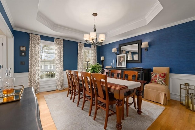 dining area featuring a tray ceiling, wood finished floors, a wainscoted wall, and a chandelier