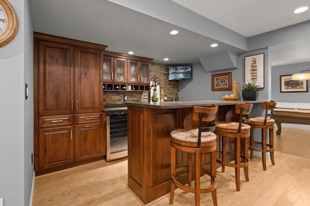 bar with indoor wet bar, wine cooler, light wood-style flooring, and backsplash