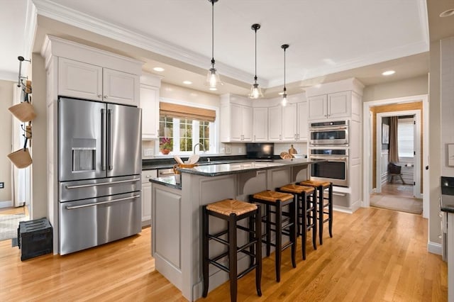 kitchen with ornamental molding, stainless steel appliances, white cabinets, dark countertops, and light wood-type flooring