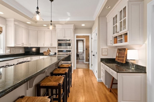 kitchen with decorative light fixtures, a breakfast bar area, white cabinets, glass insert cabinets, and a raised ceiling