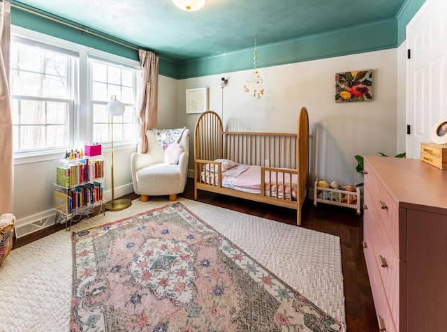 bedroom featuring dark wood-style flooring, visible vents, a textured ceiling, a nursery area, and baseboards