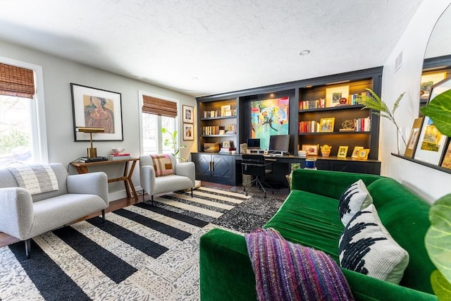 sitting room with built in features, visible vents, a textured ceiling, and wood finished floors