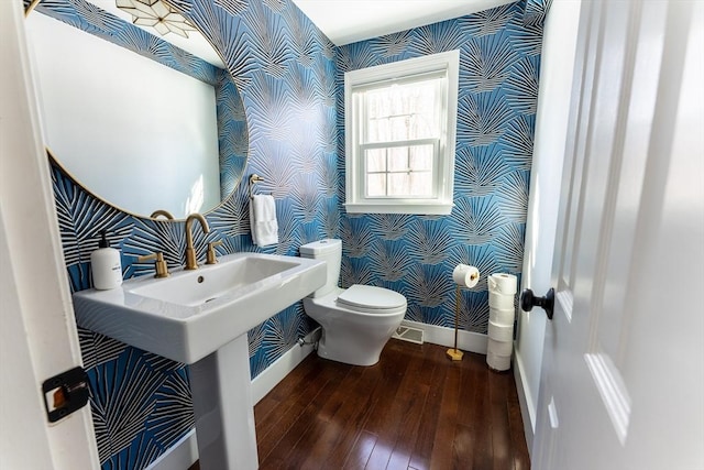 bathroom with baseboards, wood finished floors, toilet, and wallpapered walls