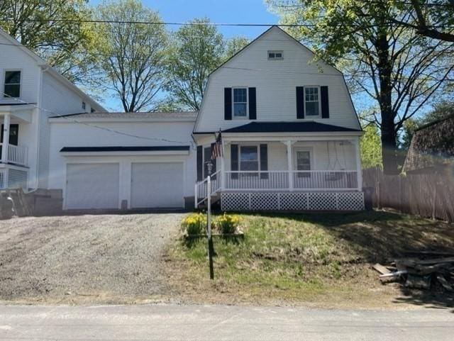 dutch colonial featuring a porch, dirt driveway, a garage, fence, and a gambrel roof