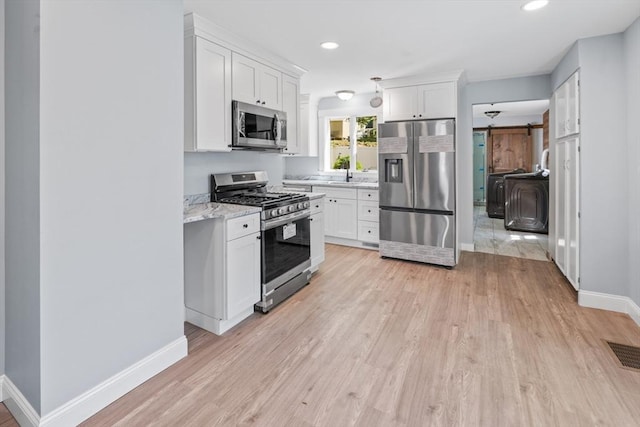 kitchen featuring visible vents, a barn door, light wood-style flooring, and stainless steel appliances