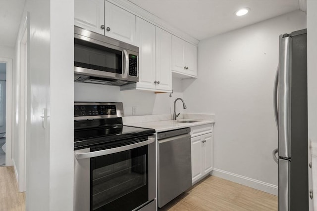 kitchen featuring appliances with stainless steel finishes, a sink, light wood-style flooring, white cabinets, and light countertops