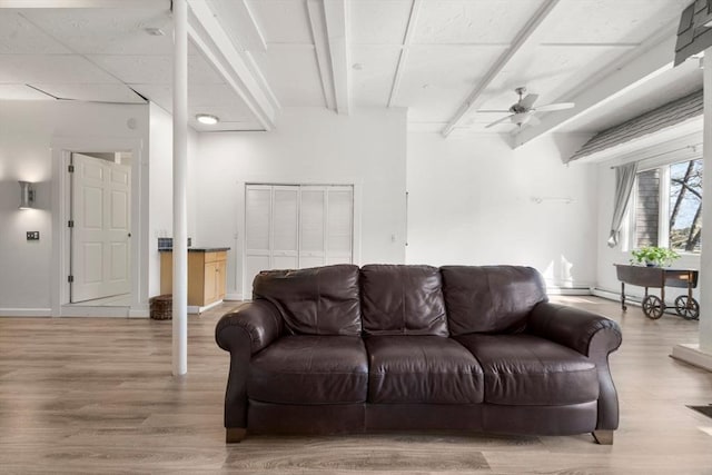 living area with a ceiling fan, light wood-style floors, beamed ceiling, and baseboards