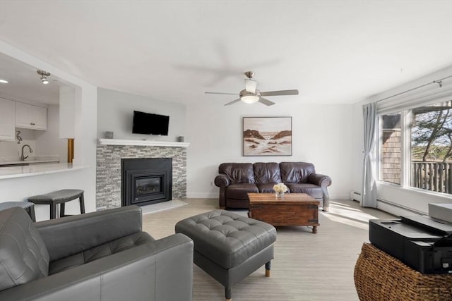 living room featuring ceiling fan, a fireplace, baseboards, and light wood finished floors