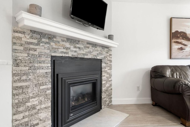 detailed view of a glass covered fireplace, baseboards, and wood finished floors