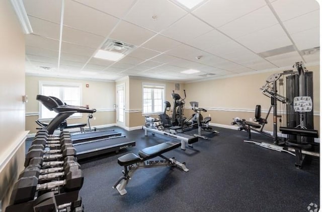 gym featuring baseboards, a drop ceiling, and plenty of natural light