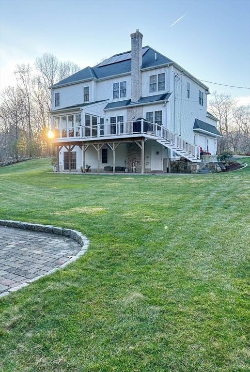 back of house featuring stairs, a deck, a lawn, and a chimney