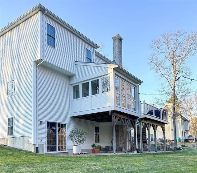 back of property featuring a patio, a lawn, a sunroom, and a chimney