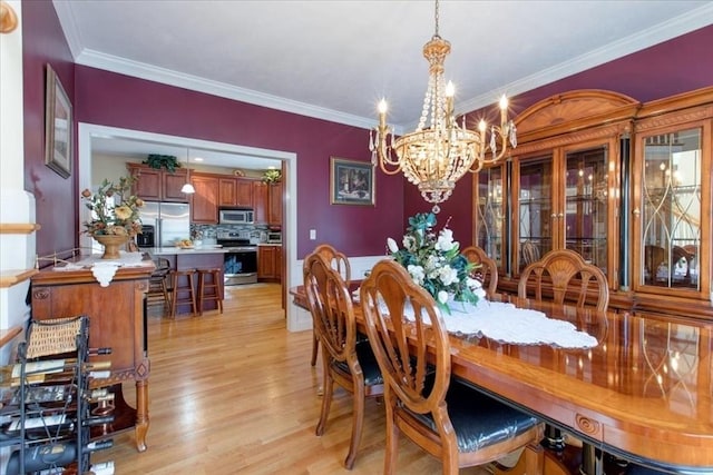 dining space with light wood-style flooring, a notable chandelier, and ornamental molding