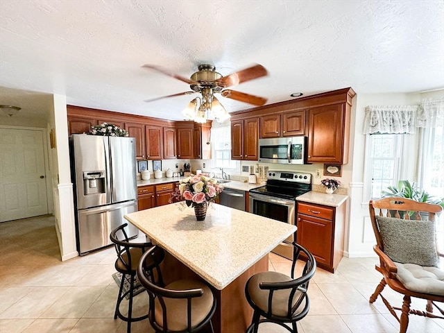 93 Mccracken Rd, Millbury, MA 01527 - kitchen featuring appliances with stainless steel finishes, a breakfast bar, ceiling fan, light tile patterned flooring, and a textured ceiling