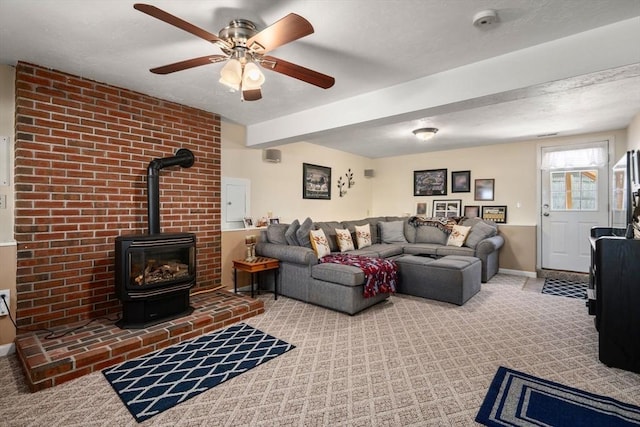 carpeted living room featuring a wood stove, a ceiling fan, baseboards, and beam ceiling