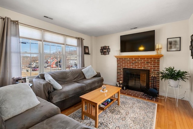 living room with a brick fireplace, wood finished floors, visible vents, and baseboards